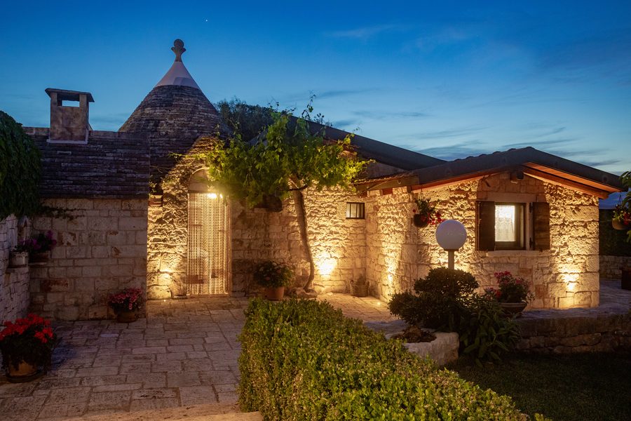 Il trullo illuminato la sera, con il cortile in pietra