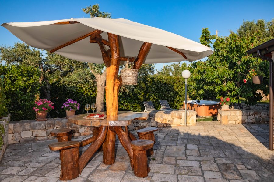 Il tavolo in legno sotto l&rsquo;ombrellone, nel cortile tra gli ulivi